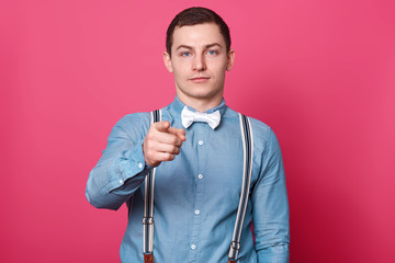 Handsome serious confident young man stands isolated over pink background in studio, rising his arm, showing direction with his forefinger, looks decisive and strong. People and emotions concept.