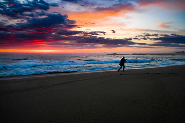 Naklejka premium Fisherman in silhouette at sunset on beach carrying fishing rod