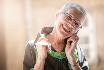 Lovely senior lady having a fun conversation with her friend or a family member over her cell phone
