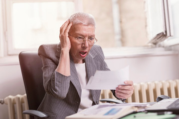 Senior old businesswoman shocked with the bills she receives, appalled and gasping