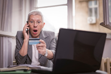 Shocked senior woman can't believe her credit card balance, arguing with the bank clerk