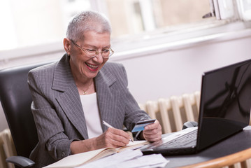 Senior elderly lady calculating her account balance, holding a credit card to do a sum up