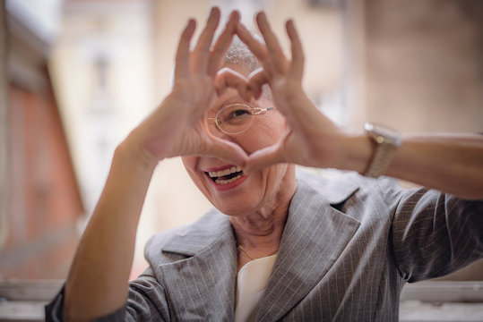 Cute senior old business woman making a heart shape with her hands and fingers