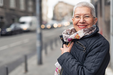 Portrait of beautiful senior woman with a jacket on a windy day in an urban city environment, happy and cheerful - 263250928