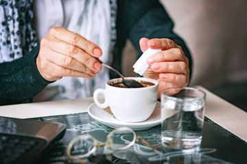 A senior old woman adding sugar to her coffee, mix and stir to blend