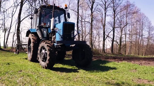 Blue tactor plows field in spring. Farming concept.