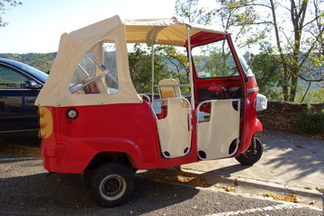 Obraz premium Funny small retro bright red three-wheeled convertible motorcycle (microcar) parked at the sidewalk (Cordes-sur-Ciel, dept. Tarn, France. Oct. 2017)