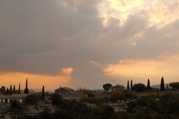 The sun's rays in the sunset sky breaking through the thunderclouds under an old town's roofs (Gordes, France)
