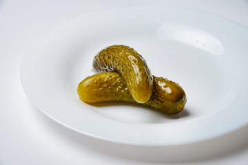 Appetizing pickled cucumbers on a white plate. White background. Side view.