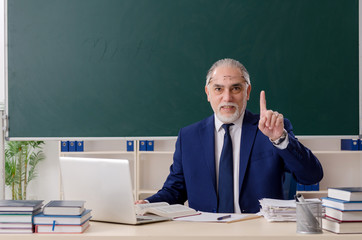Aged male teacher in front of chalkboard 