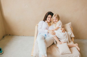 Fototapeta na wymiar Mother and daughter indoor lifestyle portrait. Mom with child have fun on abstract background. Happiness of motherhood. Mother hugs with her little daughter. Young emotional girl playing with mom.