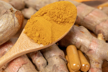 selective focus image of turmeric powder in wooden spoon,  turmeric root rhizome which some slice yellow pieces and turmeric capsule on wooden board
