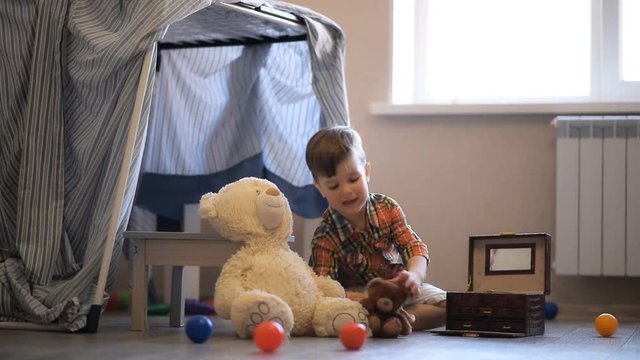 a small child built a wigwam in his room and plays there with a teddy bear