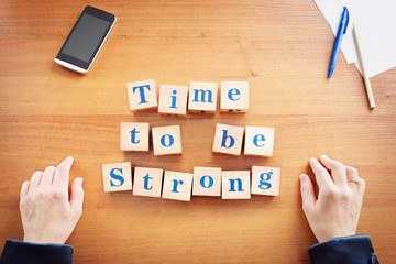 Time to be strong. Business woman made text from wooden cubes on a desk