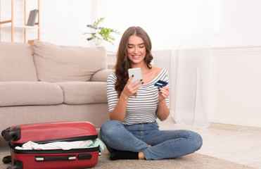 Woman booking tour online, holding phone and credit card