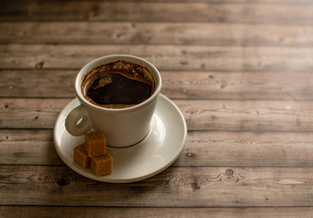 White Cup of coffee on wood natural background cane sugar pieces on plate