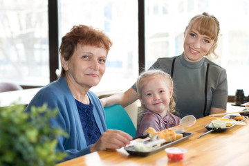 Fototapeta premium Cheerful friendly family of three women Relatives celebrate a holiday in a cafe, sit on the background of a large window.