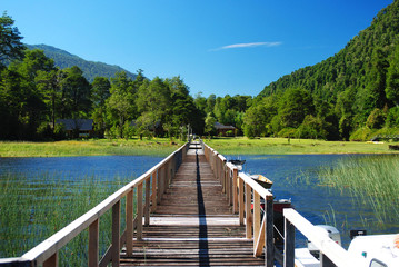 Central view of a wooden bridge at a lagoon or lake with blue cold waters, surrounded by nature, forests and mountains, in Patagonia, Chile, near Carretera Austral, ideal for fishing, on a sunny day