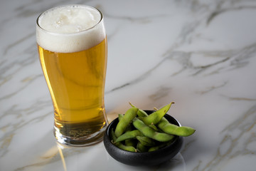 Portion grüne, japanische Edamame Sojabohnen in Porzellan Schale und Bier Glas auf Marmor Hintergrund