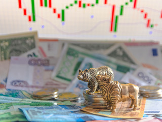 Bronze figures of a bull and a bear near metal coins against the background of paper money and...