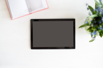 Tablet with black empty screen. Notebook and flowers on table