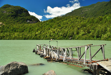 Small wooden dock for the small boats in the light green icy waters of Ventisquero lagoon, on a sunny summer morning, in Queulat National Park