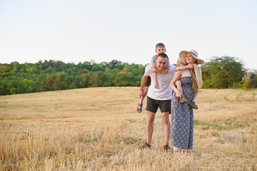 Happy young family. A father, a pregnant mother, and two little sons on their backs. Beveled wheat field on the background. Sunset time