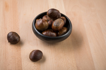 Maronen Esskastanien in schwarzer Schale auf Holz Hintergrund 