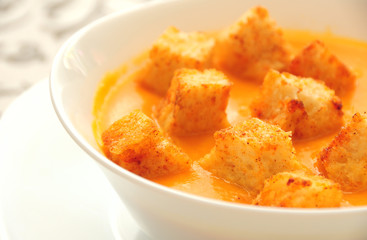 Pumpkin cream soup with spiced croutons in a white porcelain bowl