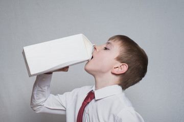 Little boy drinks from a large white package. White shirt and red tie. Light background