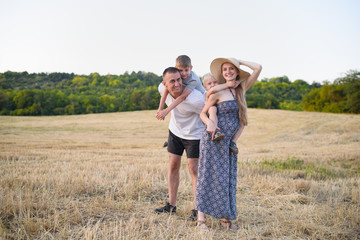 Naklejka na ściany i meble Happy young family. A father, a pregnant mother, and two little sons on their backs. Beveled wheat field on the background. Sunset time