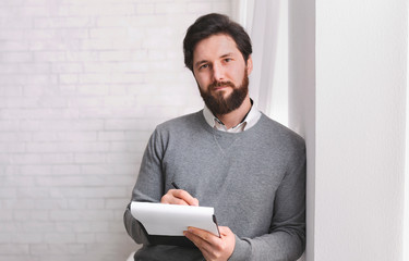 Friendly psychologist standing with clipboard, leaning at wall