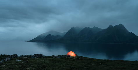 Illuminated tent at the lofoten islands on the rainy evening with copy space - obrazy, fototapety, plakaty