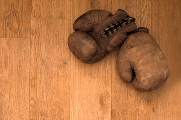 Boxing gloves. Old vintage retro pair of leather worn mittens are on the wood table. Red colors and soft lights. Gloves of retired boxer and fighter