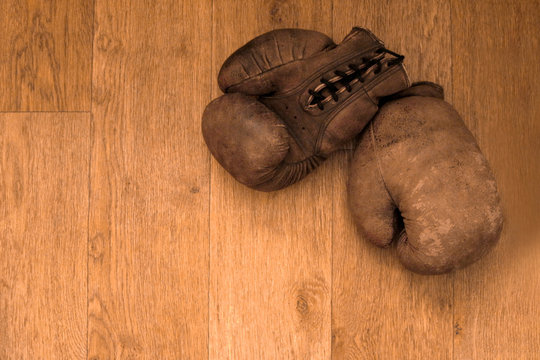 Boxing gloves. Old vintage retro pair of leather worn mittens are on the wood table. Red colors and soft lights. Gloves of retired boxer and fighter