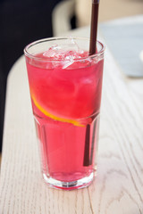 Iced rose and berries tea with lemon sliced on light brown table. Cold mocktail.