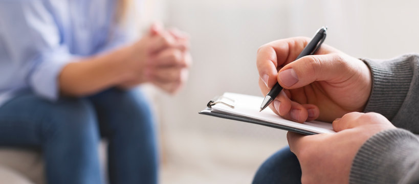 Specialist noting problems of young woman at psychotherapy session