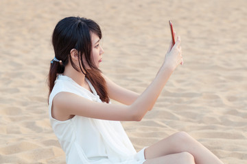 Fototapeta na wymiar Girl sitting on the beach taking a selfie