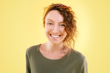 Sunny young beautiful curly woman is smiling positively and looking into the camera on a yellow background