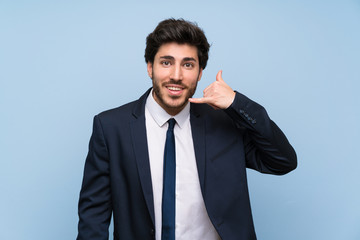 Businessman over isolated blue wall making phone gesture. Call me back sign