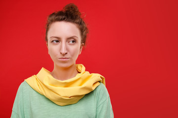 Beautiful young woman is thinking and looking to the side and is sad about something posing on a red background. Advertising space