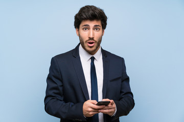 Businessman over isolated blue wall surprised and sending a message