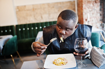 African man in black traditional clothes sitting at restaurant and eat pasta and drink wine.