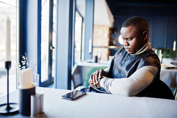 African man in black traditional clothes sitting at restaurant and looking at his watches.