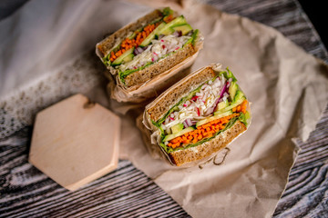 appetizing healthy vegetable sandwich in craft paper on the dark wood table.