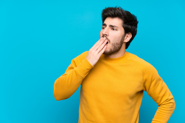 Handsome over isolated blue wall yawning and covering wide open mouth with hand