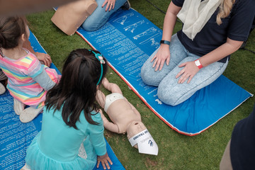 Young female first-aider demonstrating CPR to kids with dummy infant