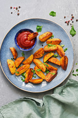 Baked fried potatoes with tomato sauce, spices and greens in a plate on a gray background. Top view, copy space.