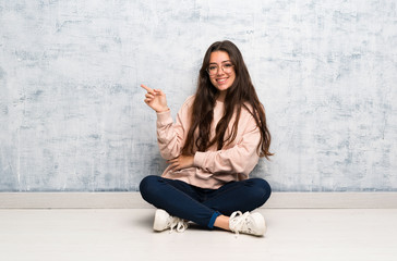 Teenager student girl studying in a table pointing finger to the side