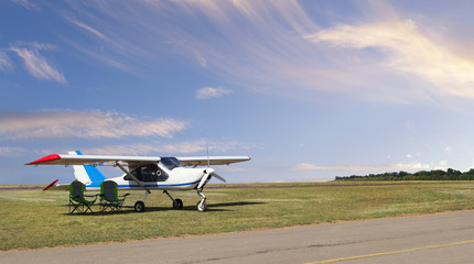 Fototapeta na wymiar Front view of light aircraft with piston engine on airfield with two folding lounge chairs under the wing against the backdrop of a calm cloudy sky